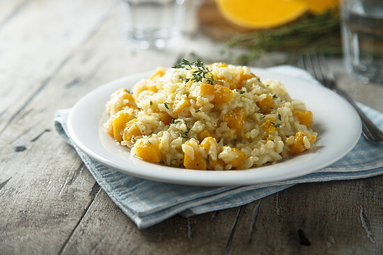 Creamy butternut squash risotto topped with thyme on a cozy, inviting plate setting.