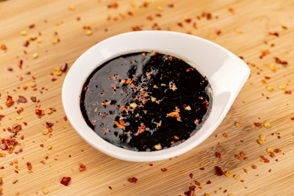 Dark chili oil with red pepper flakes in white dish, ideal for food service, wholesale distribution, and commercial kitchen applications.