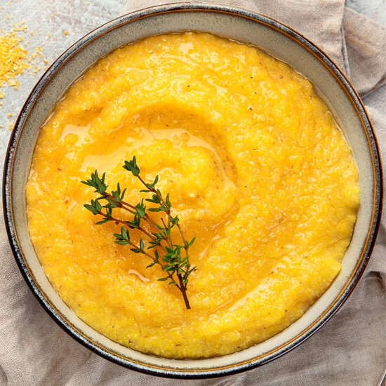 Bowl of creamy yellow polenta topped with thyme, embodying warmth and comfort in every bite.