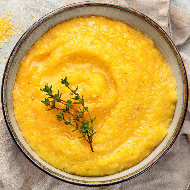 Bowl of creamy yellow polenta topped with thyme, embodying warmth and comfort in every bite.