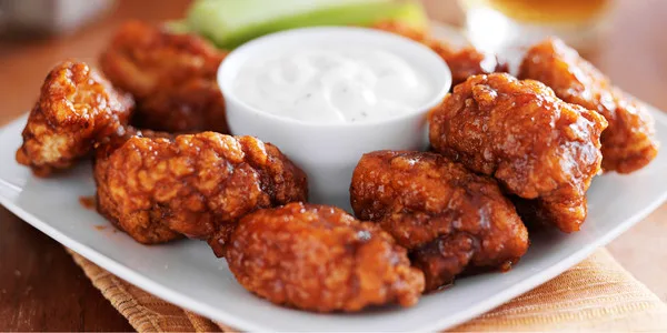 Golden-brown fried chicken wings arranged on a white plate with a white ramekin of creamy ranch dip, ideal for foodservice and wholesale distribution.
