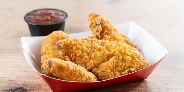 Golden fried chicken pieces in a red food service container with red sauce, ideal for wholesale food distribution and commercial foodservice suppliers.