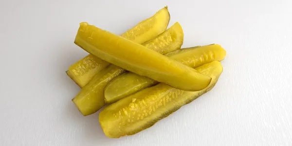 Fresh pickle spears stacked on a clean surface, showcasing vibrant yellow-green color and glossy texture.