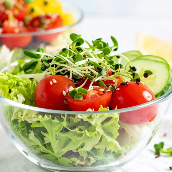 Vibrant fresh salad with mixed greens, cherry tomatoes, and cucumbers in a glass bowl.