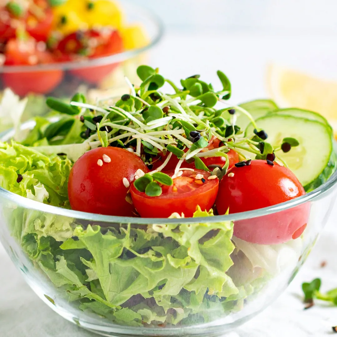 Vibrant fresh salad with mixed greens, cherry tomatoes, and cucumbers in a glass bowl.
