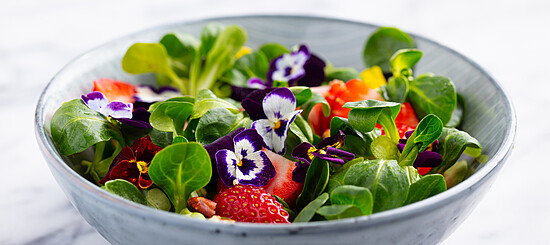 Colorful salad with strawberries and edible flowers in a matte bowl. Fresh and vibrant.
