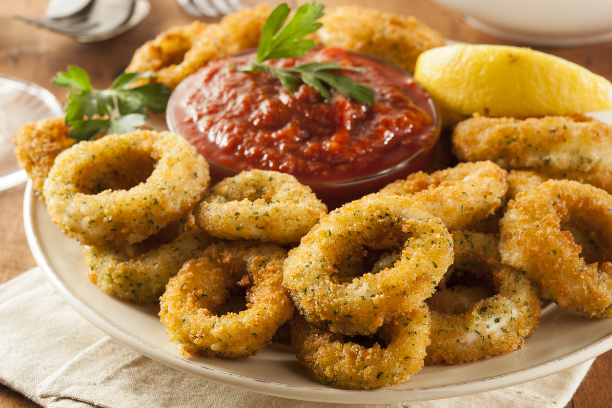 Crispy fried calamari with marinara sauce and lemon wedge on a rustic wooden table.