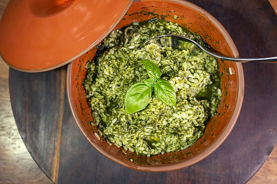 Creamy green risotto garnished with basil, served in a rustic terracotta pot.