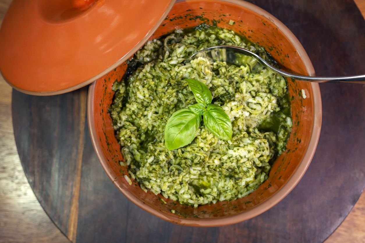 Creamy green risotto garnished with basil, served in a rustic terracotta pot.