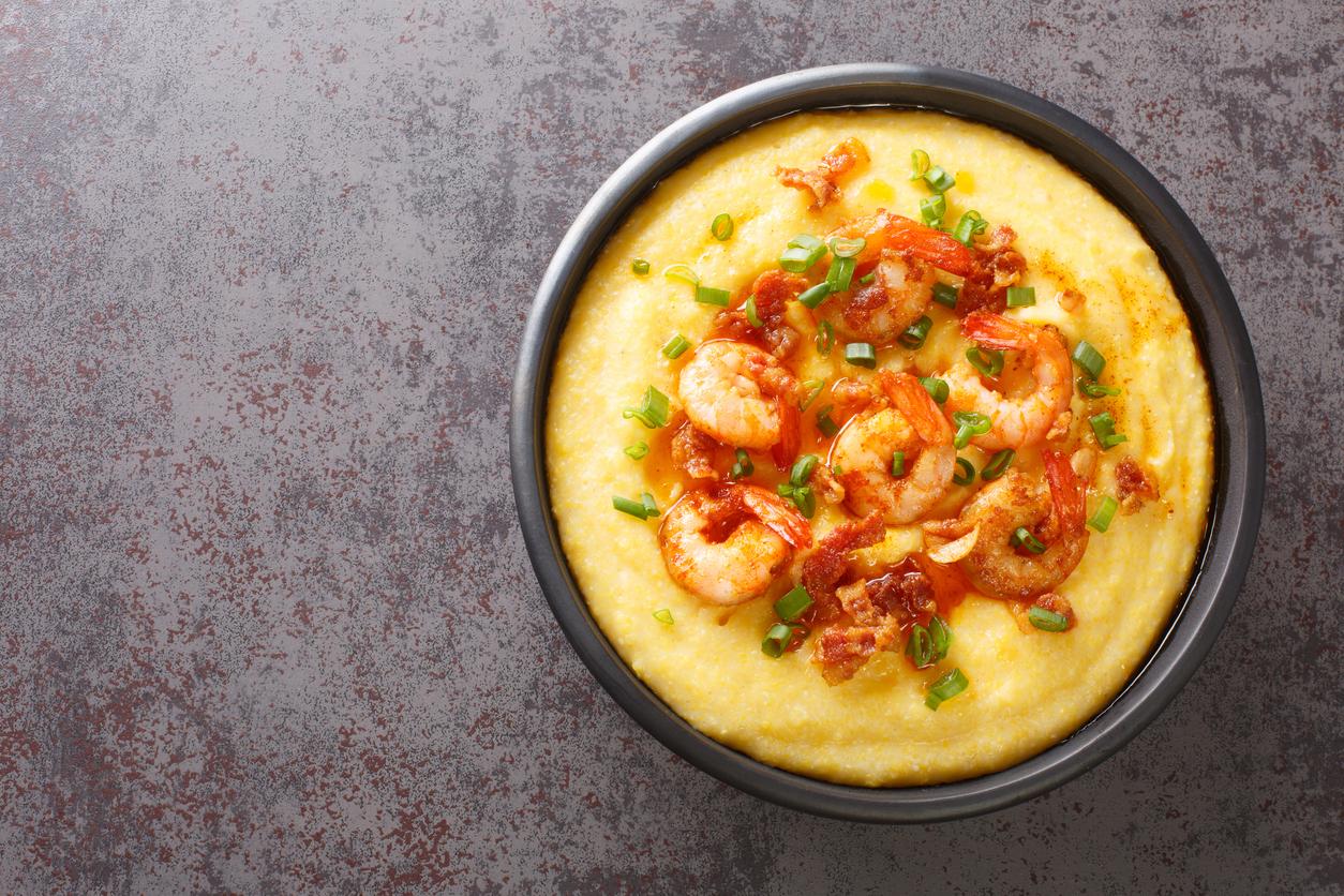Homemade Shrimp And Grits With Smoked Bacon, Onions And Cheese In A Black Bowl On A Dark Concrete Background. Horizontal Top View