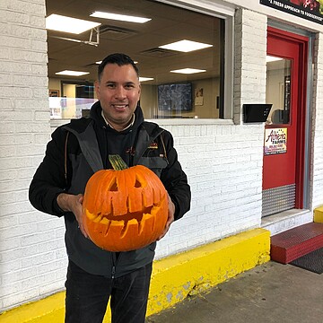 Man holds a bright jack-o-lantern outside Altena Farms, celebrating autumns festive spirit.