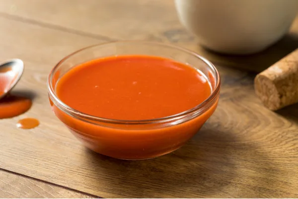 Commercial-grade red hot sauce in clear glass bowl on wooden surface, ready for food service and wholesale distribution.