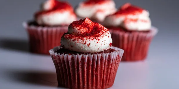 Professional red velvet cupcakes with white frosting and red sparkle garnish in commercial bakery packaging for food service distribution.