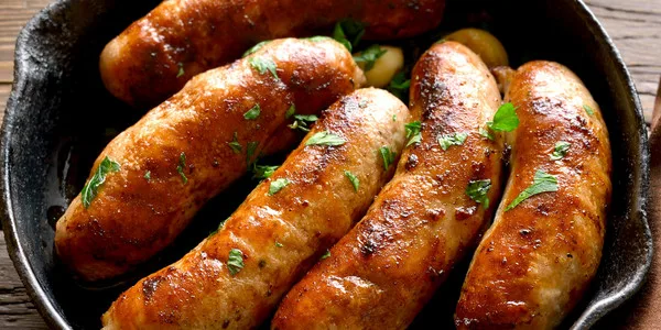 Golden-brown sausages sizzling in a cast iron skillet, ideal for wholesale food distribution and foodservice suppliers.