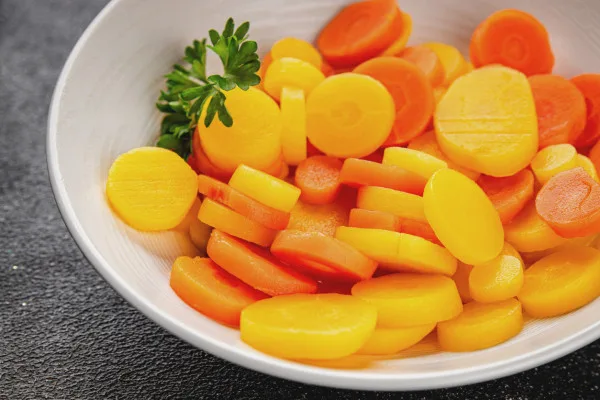 Sliced orange and yellow carrots arranged on a white plate, ideal for wholesale food suppliers and foodservice distribution.